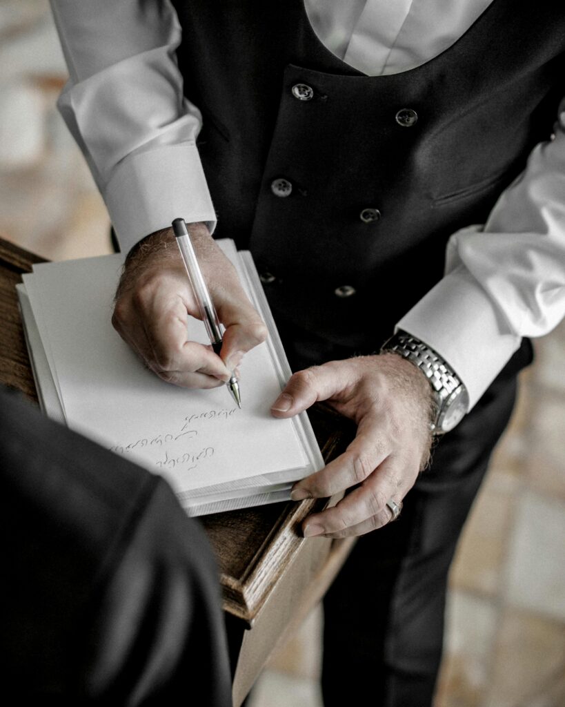 Homem de terno escrevendo em documento sobre mesa de madeira, representando assinatura de contrato.