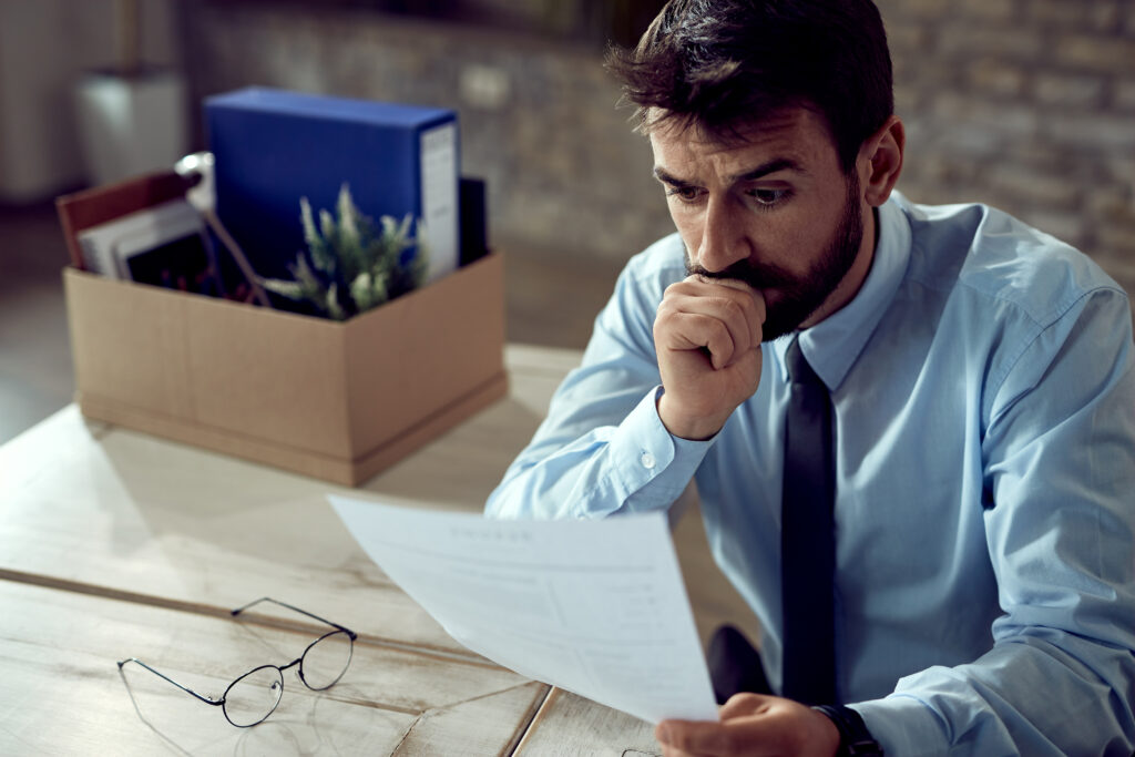 Empresário analisando documentos trabalhistas em uma mesa, com expressão preocupada e um gráfico financeiro ao fundo.